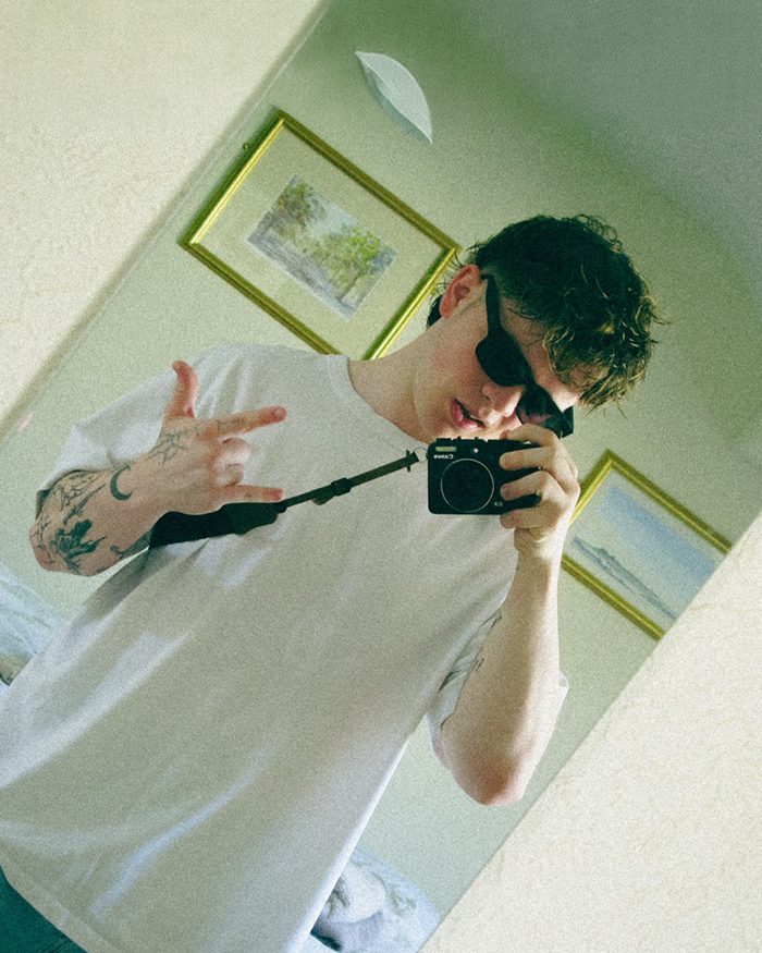 Cole taking a mirror selfie on a compact film camera, throwing a peace sign.