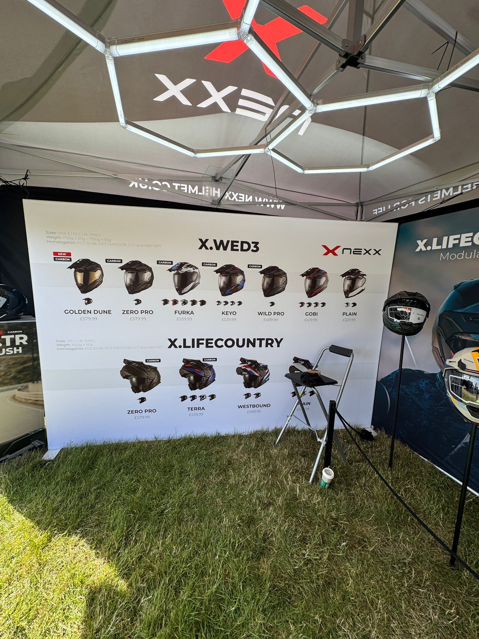 NEXX event stand at a show, printed product wall listing the X.WED3 and X.LIFECOUNTRY ranges.